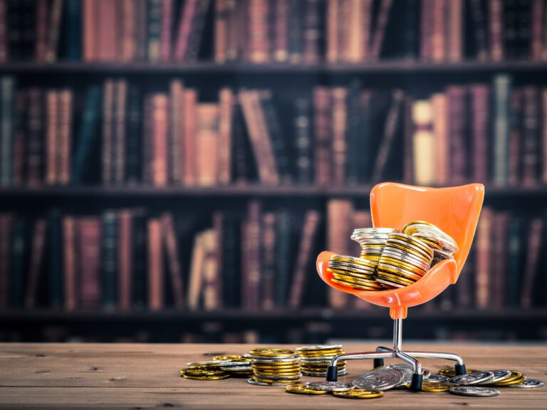 Auf einem Miniatursessel liegen Münzen, im Hintergrund ein Buchregal