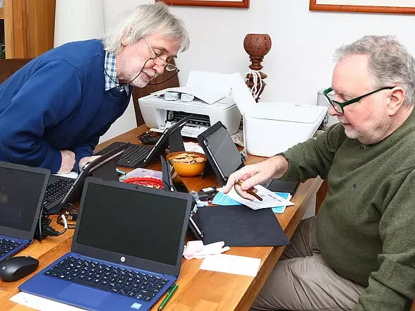 Zwei Männer beugen sich über mehrere Notebooks.