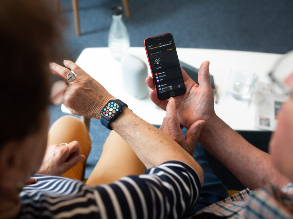 Zwei Menschen schauen auf eine Smartwatch und ein Smartphone