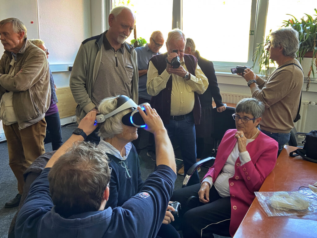 Eine Gruppe Älterer testet eine VR-Brille und wird dabei fotografiert.