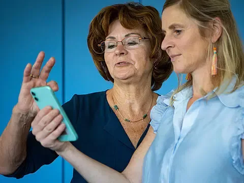 Zwei Frauen in unterschiedlichem Alter schauen auf ein Smartphone.