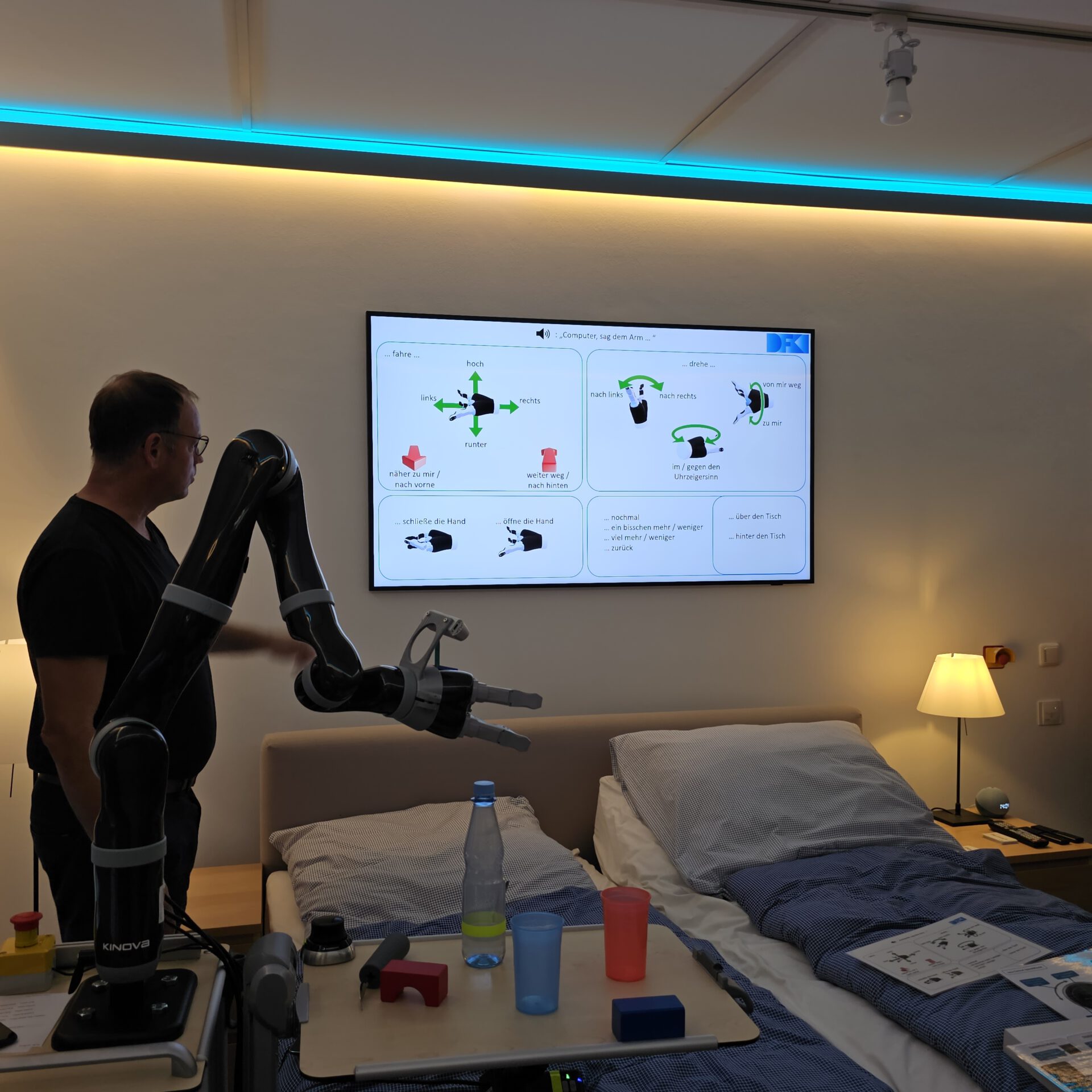 Ein Greifarm, im Hintergrund Bildschirm mit Sprachbefehlen