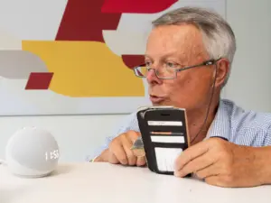Mann spricht mit smarten Lautsprecher und hat ein Smartphone in der Hand