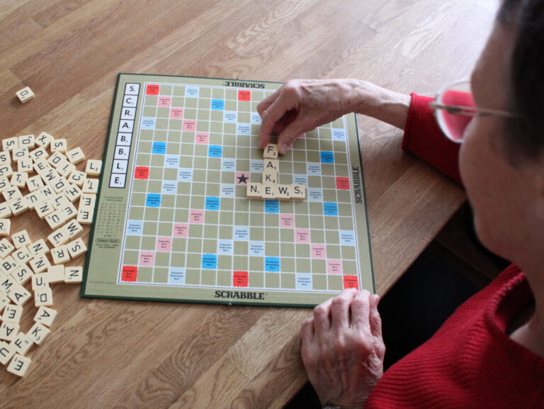 Ältere Frau legt auf einem Scrabble Brett das Wort Fake News