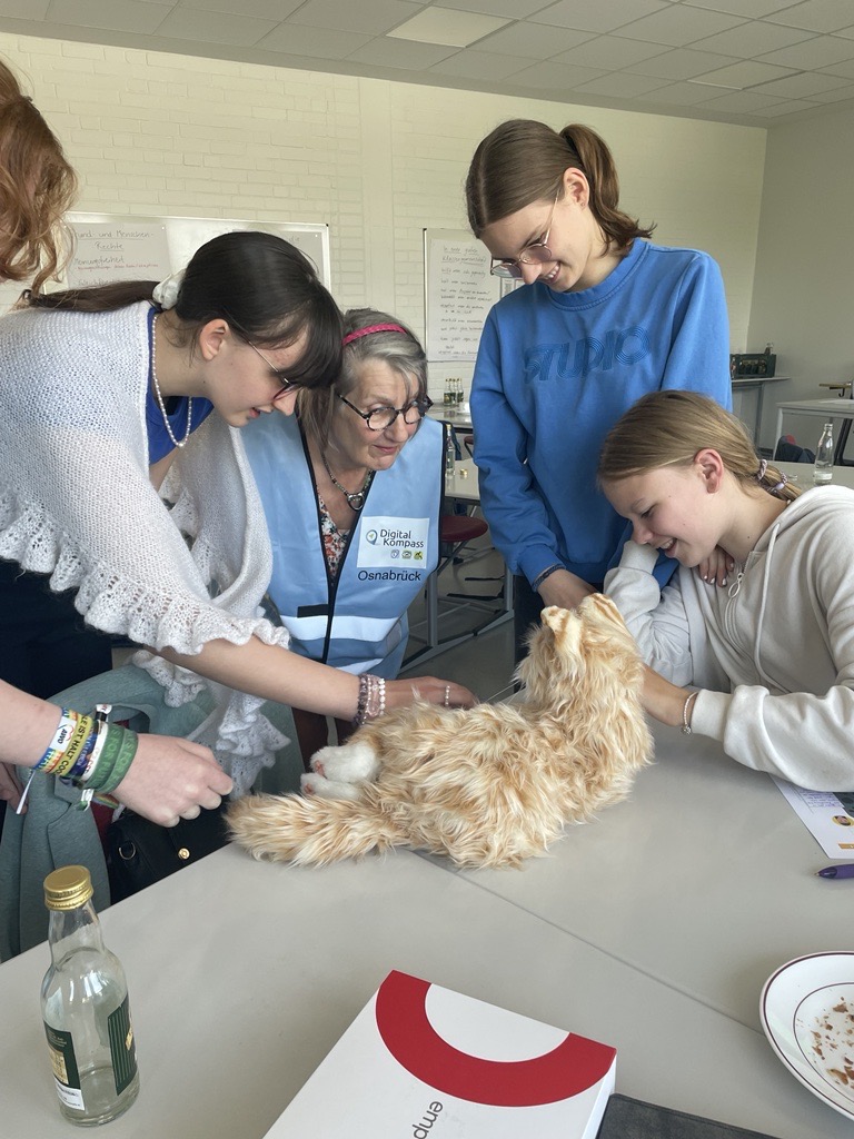 mehrere Schülerinnen und eine ältere Frau spielen mit einer Roboterkatze