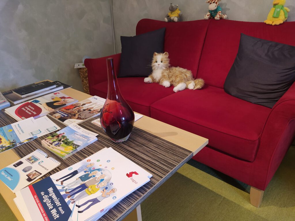 Sofa auf der eine Roboterkatze sitzt, davor ein Tisch mit verschiedenen Broschüren