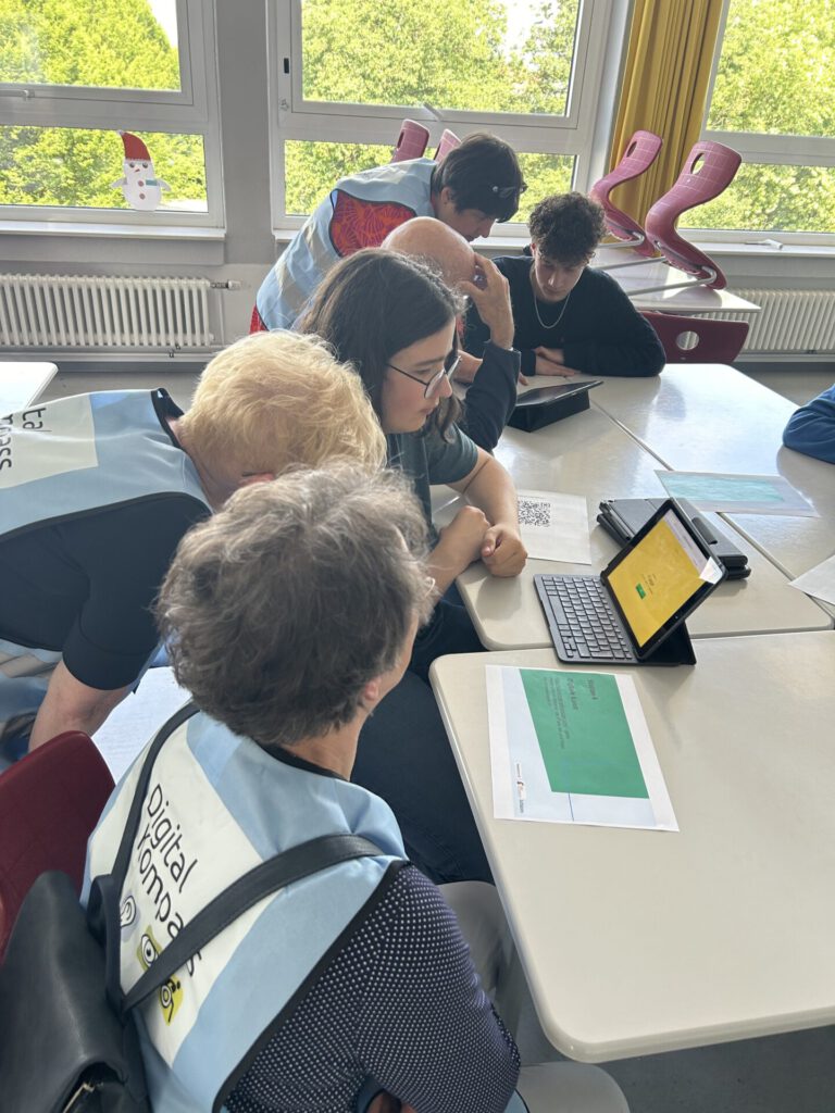 mehrere ältere Menschen und Schülerinnen und Schüler schauen auf zwei Tablets