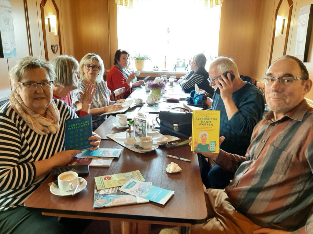 mehrere ältere Menschen sitzen an einem Tisch und haben Infomaterialien vom Projekt KI und Alter in den Händen