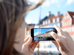 Frau fotografiert Hafen und Promenade Nyhavn in Kopenhagen, Dänemark mit Kamera von Smartphone